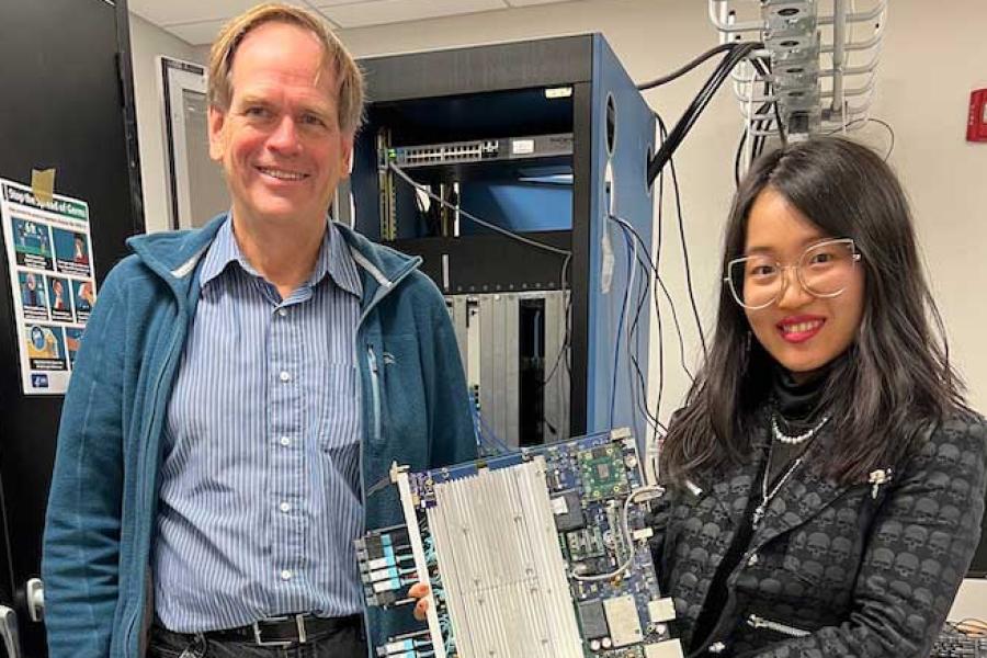 Two people hold a laptop-sized piece of equipment