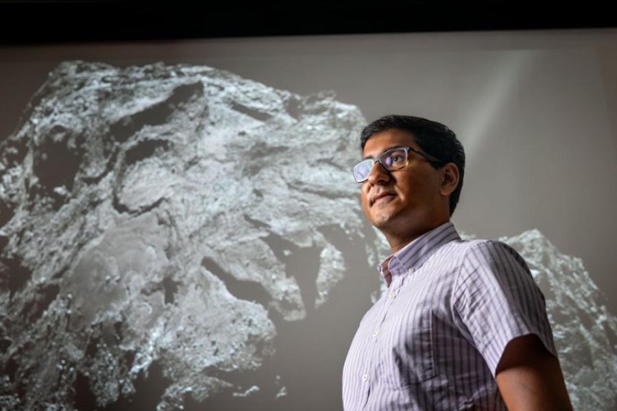 Person standing in front of a huge black & white image of a comet with a rocky surface