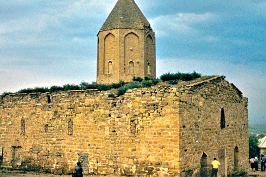 Ancient stone building with a spire and foliage growing on the roof