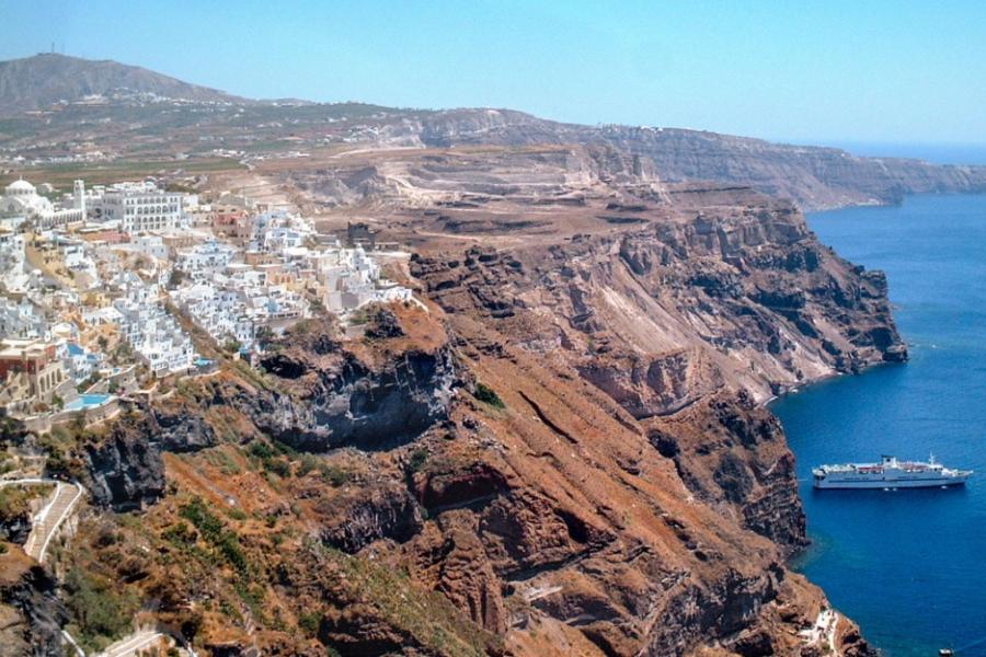 Red cliffs reaching down to blue ocean; a city of white buildings appears small
