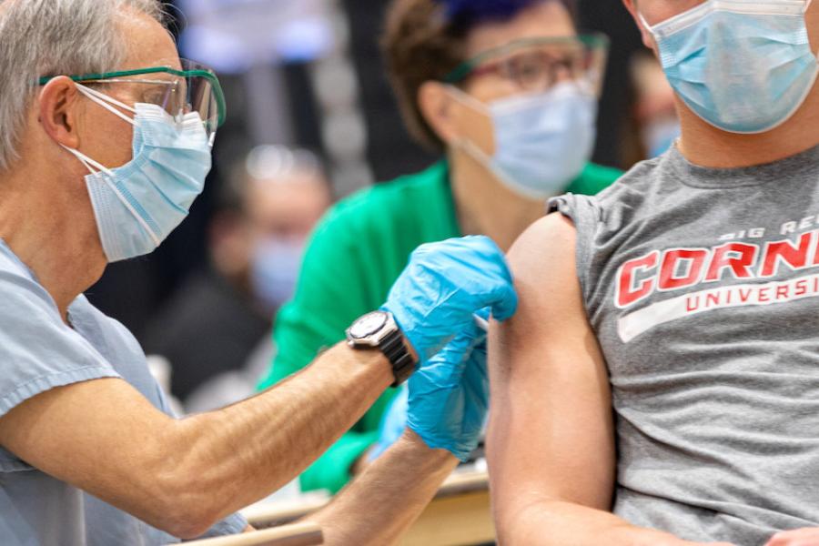Medical professoional wearing a mask and protective gloves gives a shot to a person wearing a Cornell Big Red t-shirt