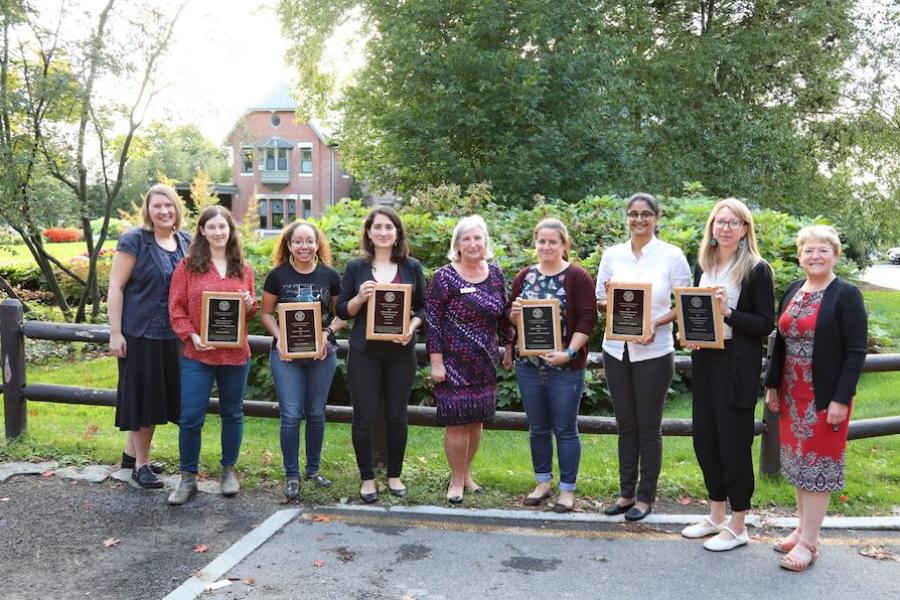 Nine people stand in a line; six of them hold plaques