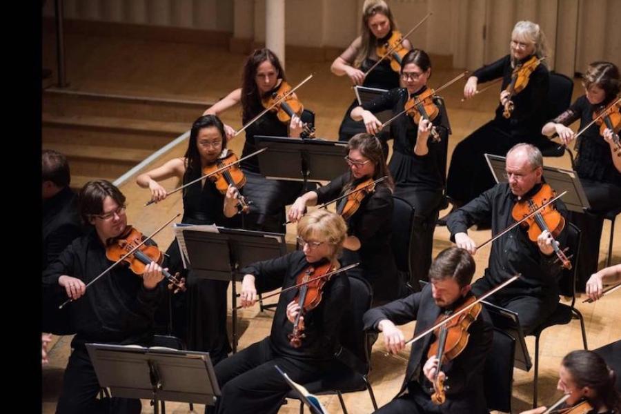 Several people arranged on a stage, playing violins