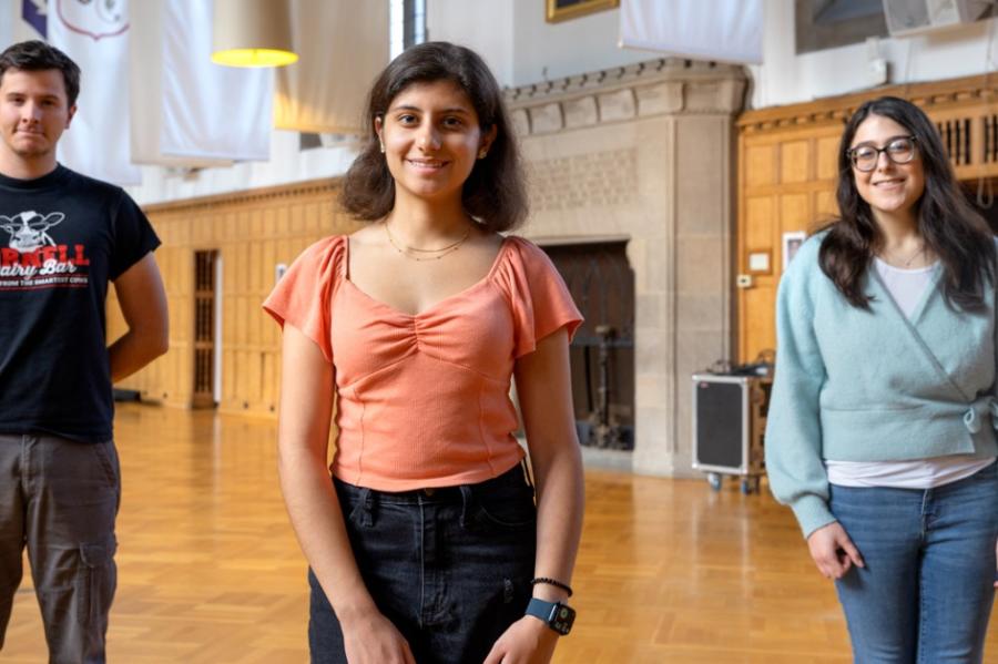 Three young people stand in a wood-paneled room