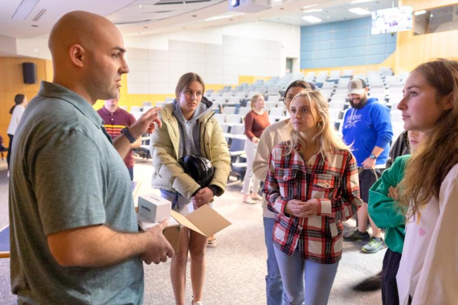 Six people stand in a group at the front of a classroom, conversing