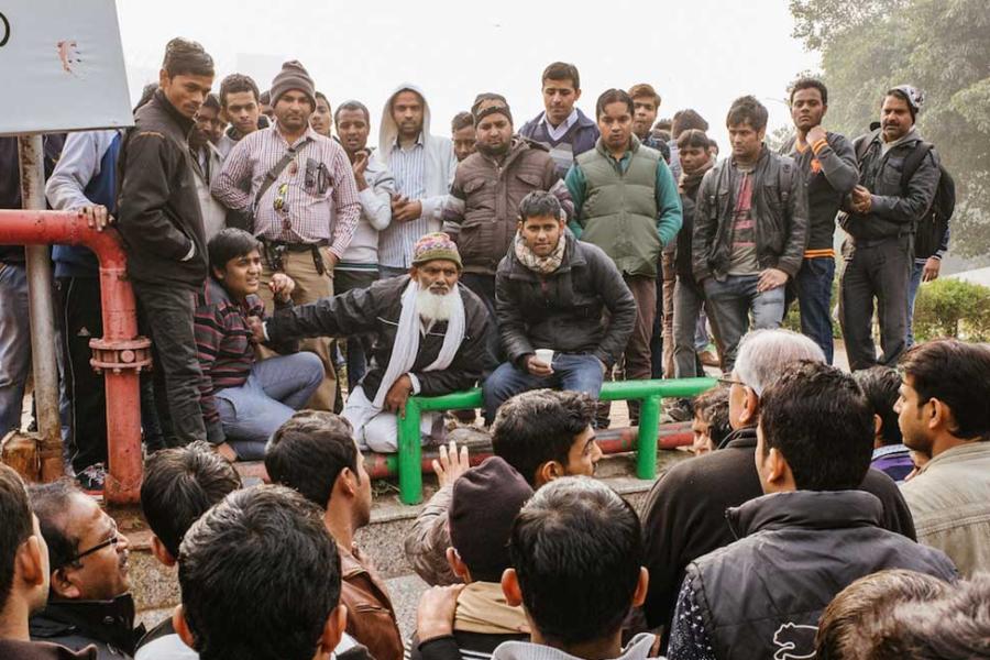 A few dozen men sit and stand in a group, talking intensely