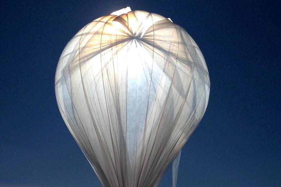 Light shines through gossamer fabric of a large, inflated balloon against a dark sky