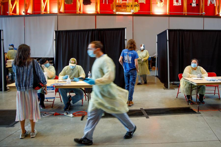 Person waits for a COVID test while people wearing medical gear hurry by