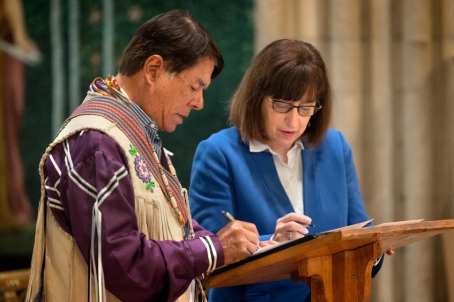 Two people sign a document on a podium