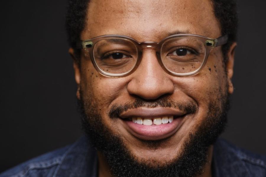 Vinson Cunningham, an African American man with black beard and brown glasses wearing a black shirt and jean jacket.
