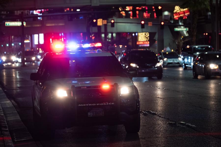 A police vehicle at night, red and blue lights reflecting off wet pavement