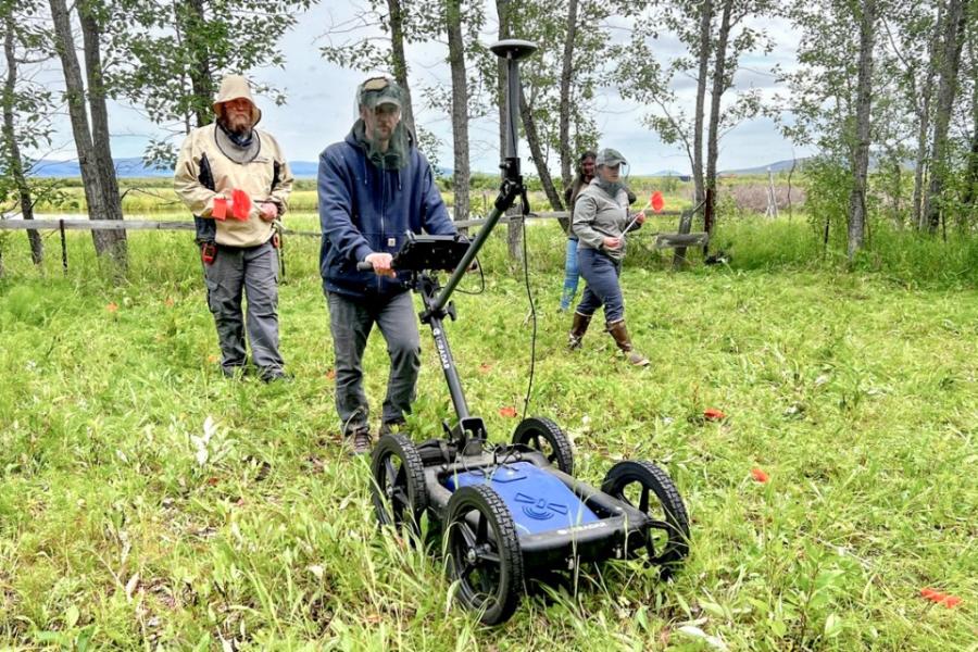 three people use a wheeled machine on a grassy plot of land