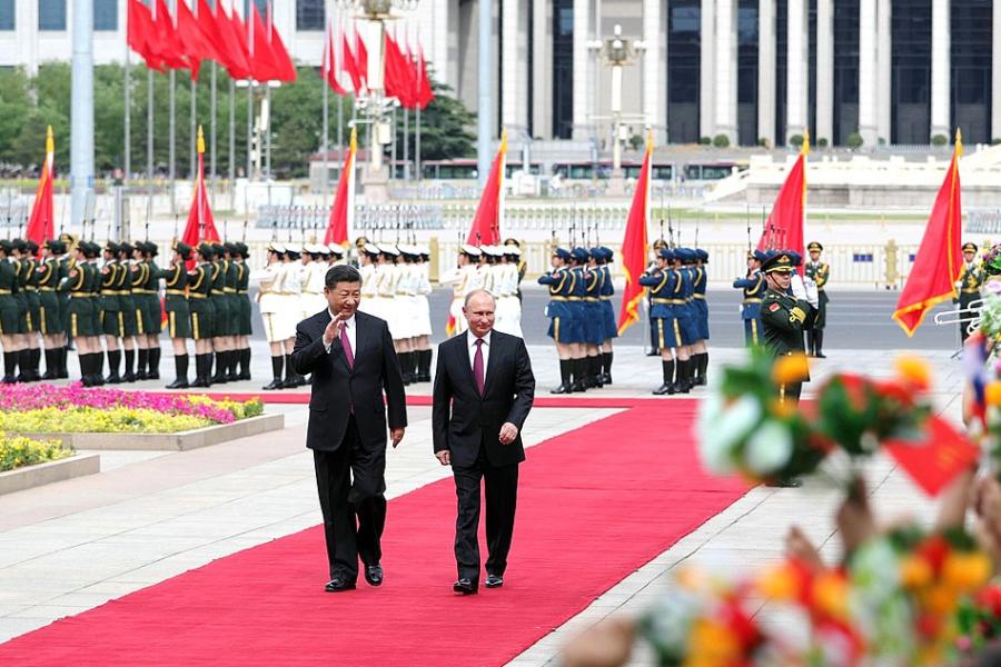 Two people wearing suits walk side by side down a red carpet, waving