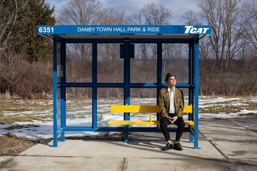Person in plaid jacket sits at a bus stop