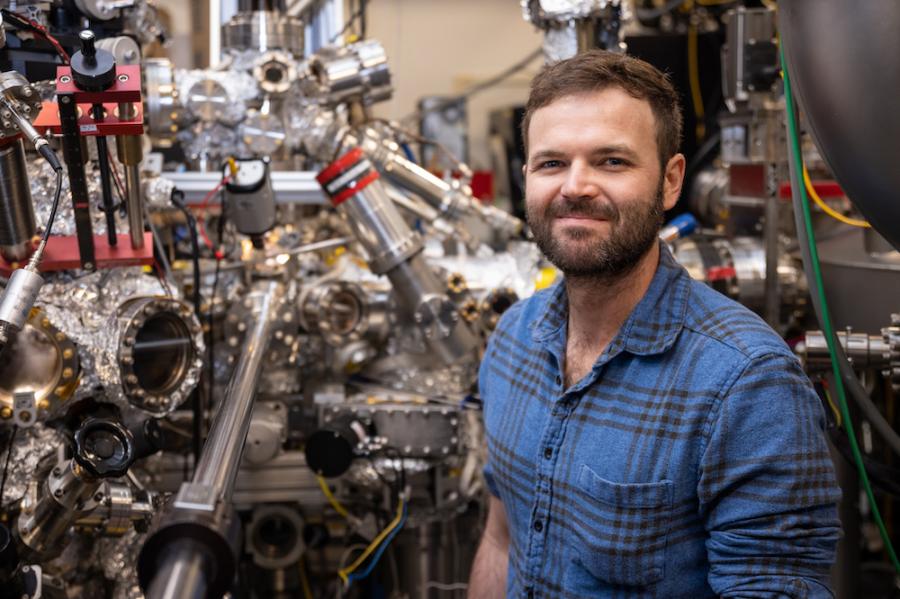 person wearing blue shirt stands in front of complicated silver equipment