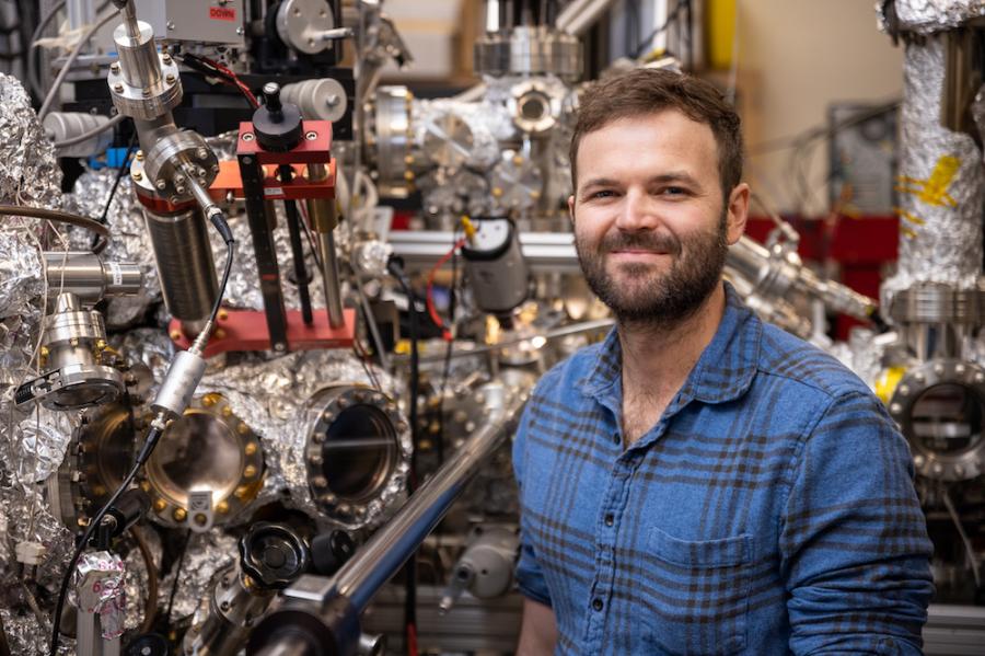 Person in blue shirt stands in front of complicated silver equipment