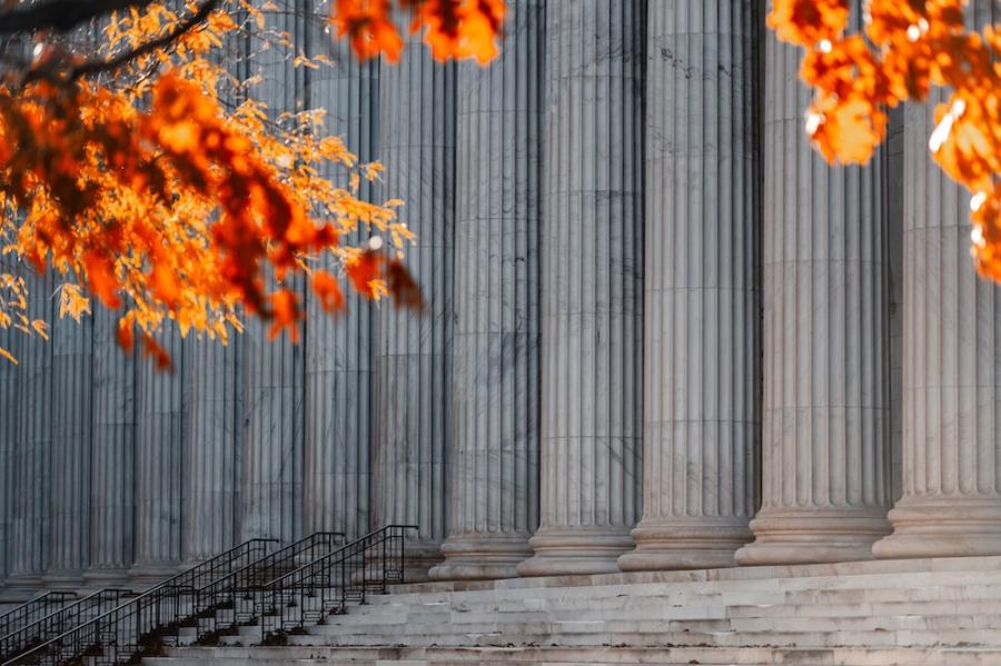Red, sun-lit leaves foreground massive stone pillars on a court building