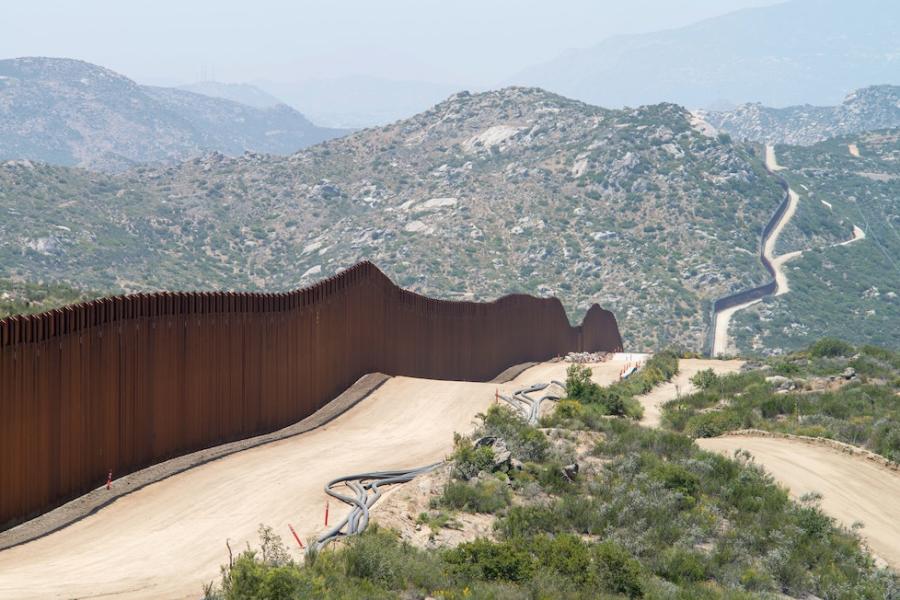 a tall fence and a dirt road go over dry hills
