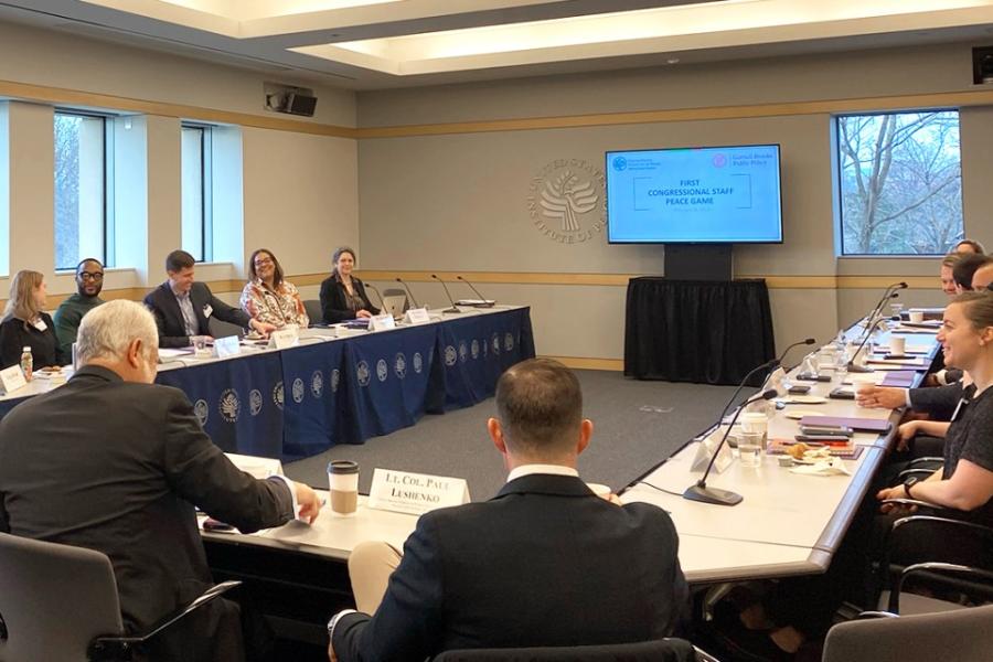 About 20 people sit at long tables arranged in a horseshoe shape