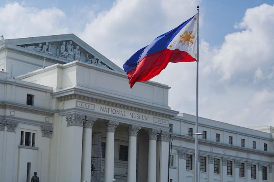 Motorcycle drives past a stone "National Museum" fronted by the Philippine flag