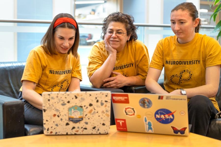 Three people wearing matching yellow t-shirts look at two laptop computers