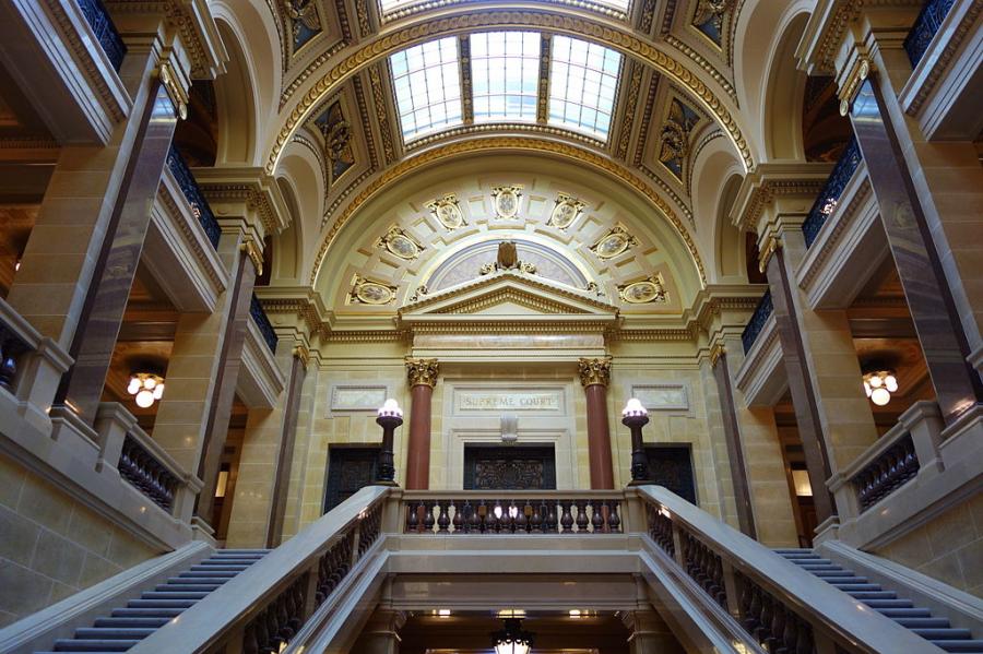 Grand building interior, two staircases lead up to a door framed by columns
