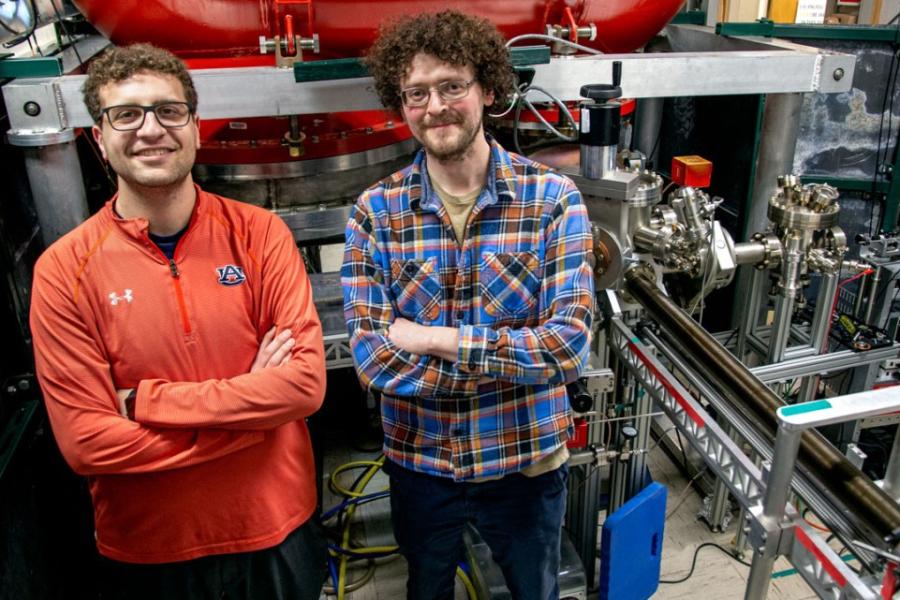Two people stand with crossed arms in front of a large, complicated machine