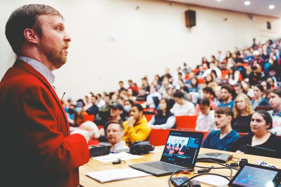 Person in red jacket speaks to a full auditorium
