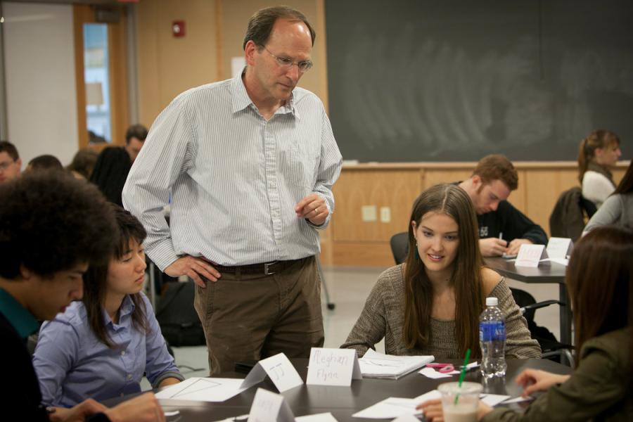 Steven Strogatz standing next to a table of students who are working on a math problem