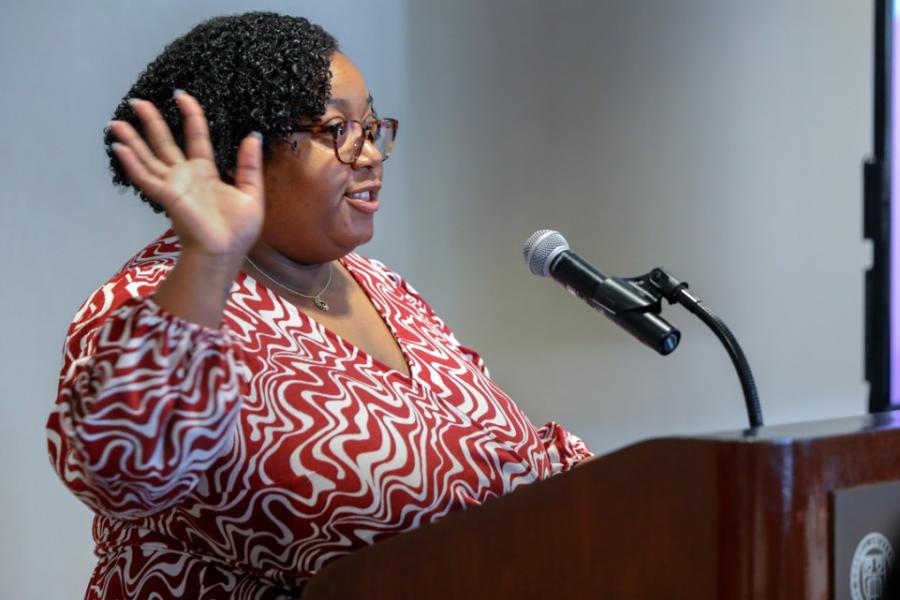 Person speaks at a podium, gesturing with one hand
