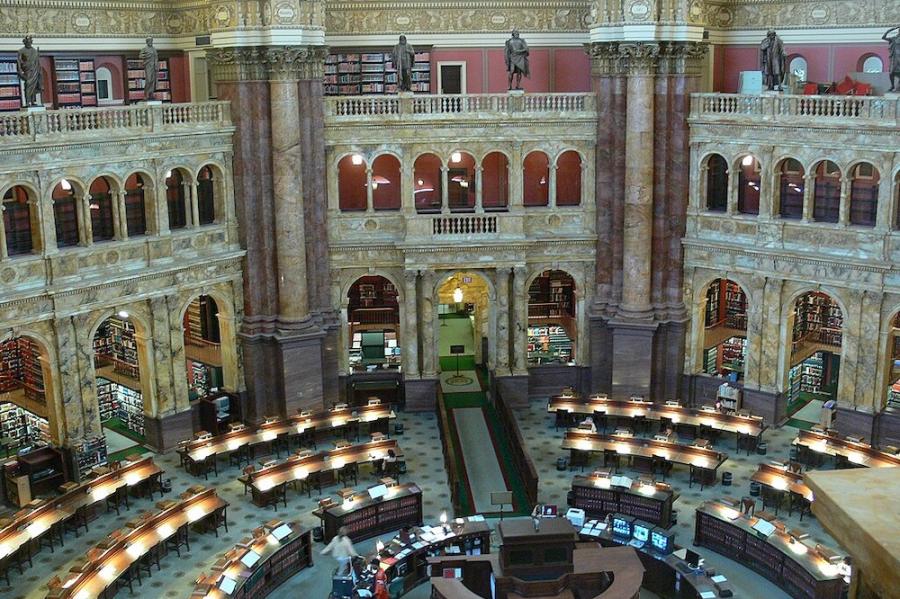 Interior of a grand building with a central desk and arched opening along the sides; book shelves