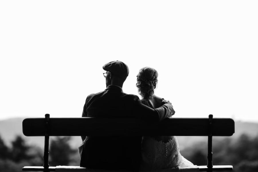 Black and white image of two people sitting on a bench, seen from behind
