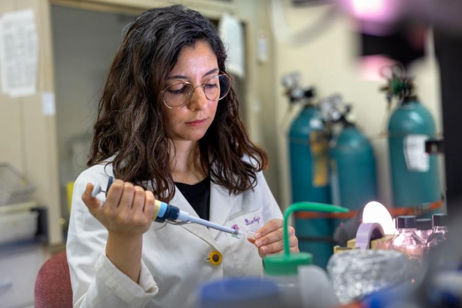 Person in a white lab coat piping something into a test tube