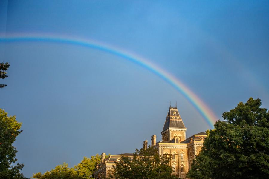 A rainbow against a deep blue sky, over a brick building with a peaked roof