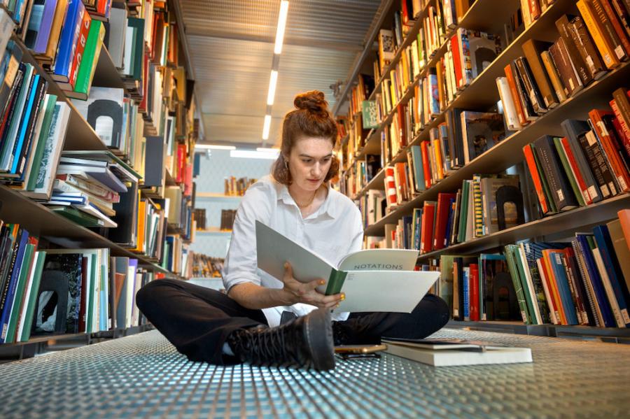 Person sitting on a floor surrounded by books on shelves