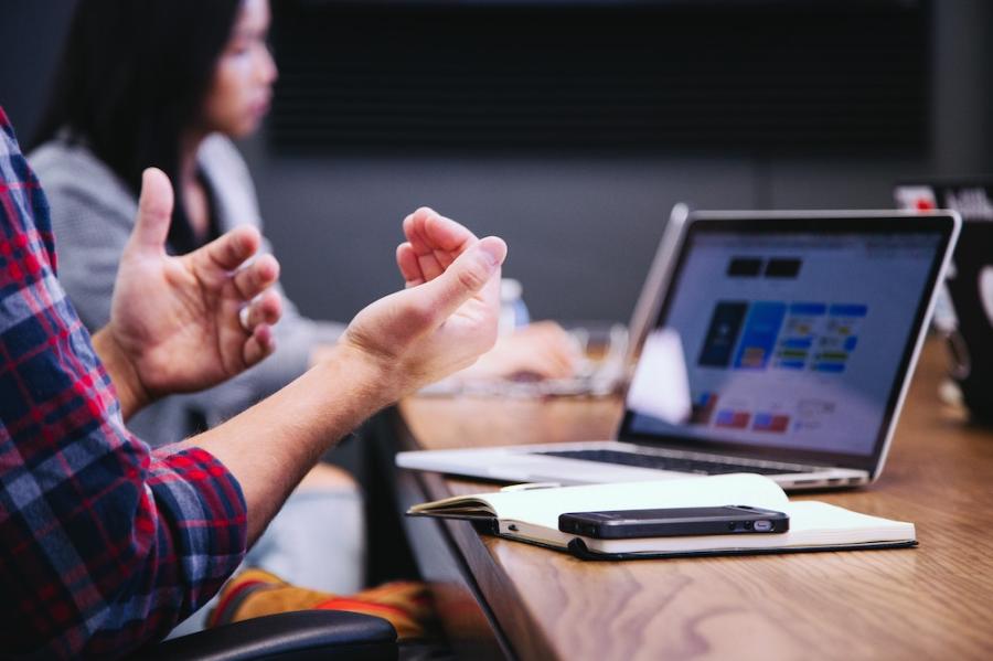 Hands gesturing in front of a laptop computer and a notebook