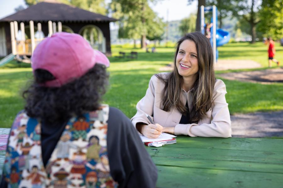 Two people sitting at a table, conversing in a shady area of a park