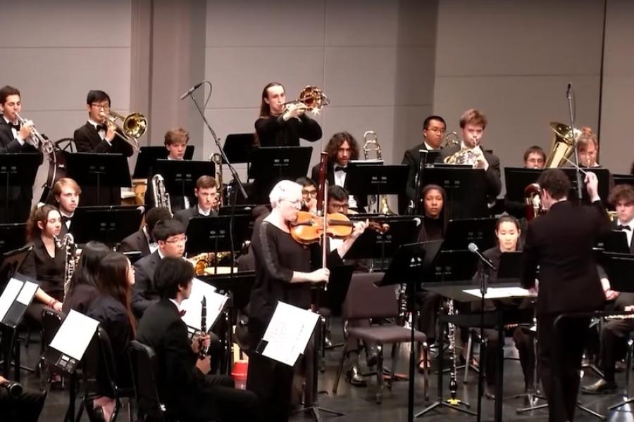 musicians playing their instruments on a stage, seated or standing behind music stands