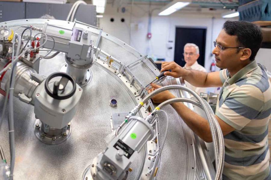 Amit Vishwas uses a screwdriver to work on ALPACA, a round metal top with metal boxes and cables protruding