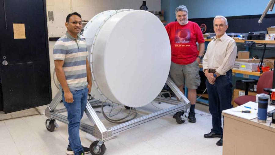 The three scientists standing around the closed and completed instrument, a flat white metal drum on a metal stand