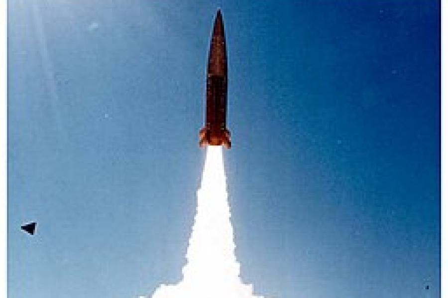 A missile on a column of smoke as it is launched into the blue sky.