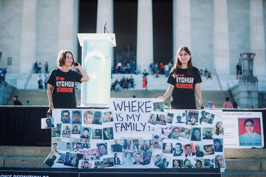 Two young people standing behind a large sign filled with snapshots of people