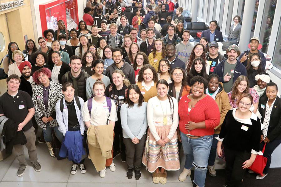 Several dozen people crowd together, looking up at the camera