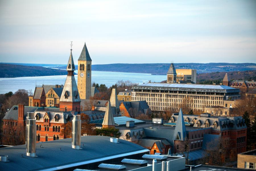 Overhead view of Cornell's campus buildings under a light sky, with a lake in the distance
