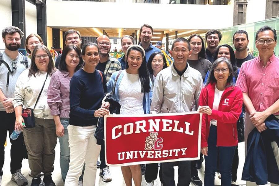 Several people stand together behind a "Cornell University" banner