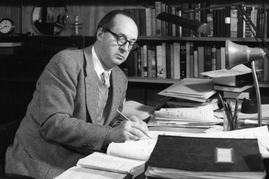 Historic black and white image: a person sitting at a desk, writing
