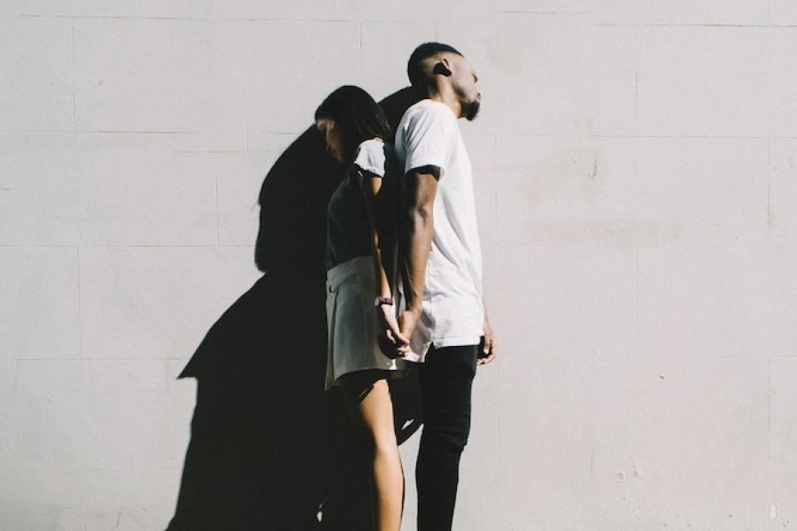 Two people leaning back to back against a wall, shadowed