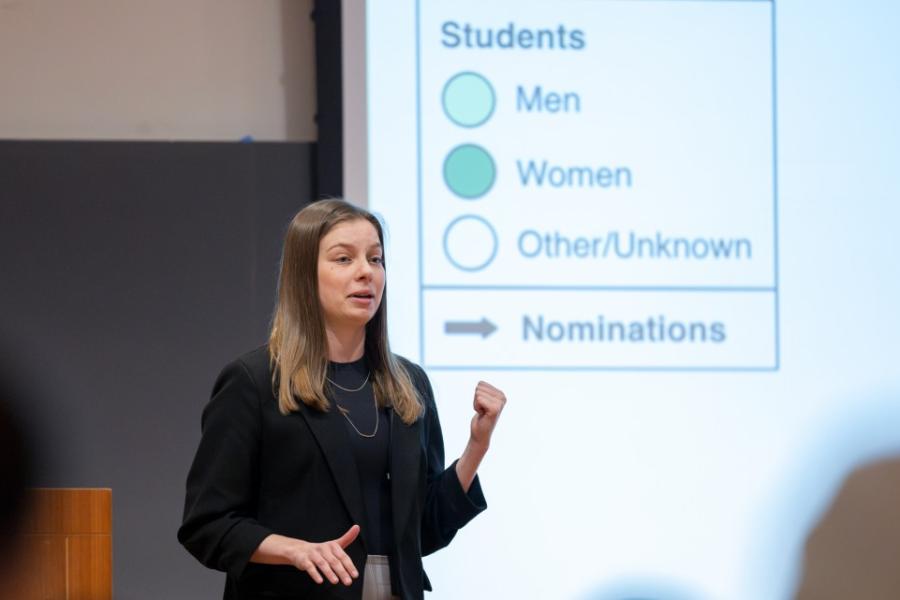 Person speaking to a group, with an illuminated screen behind