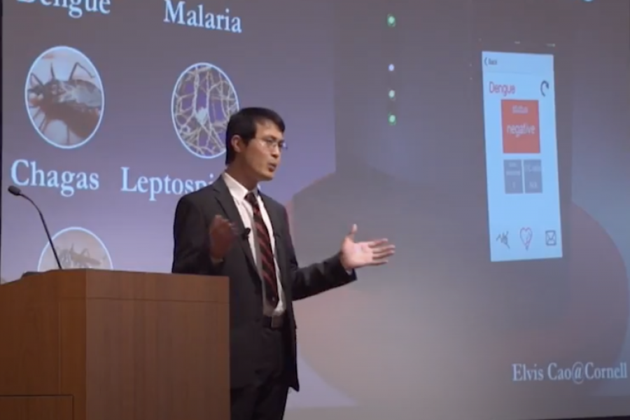 Person speaking at a podium in front of a screen illuminated with a scientific image