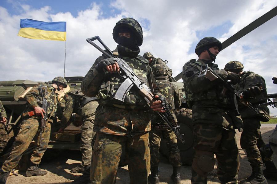 Several soldiers cluster near a tank; a blue and yellow Ukraine flag flies nearby 